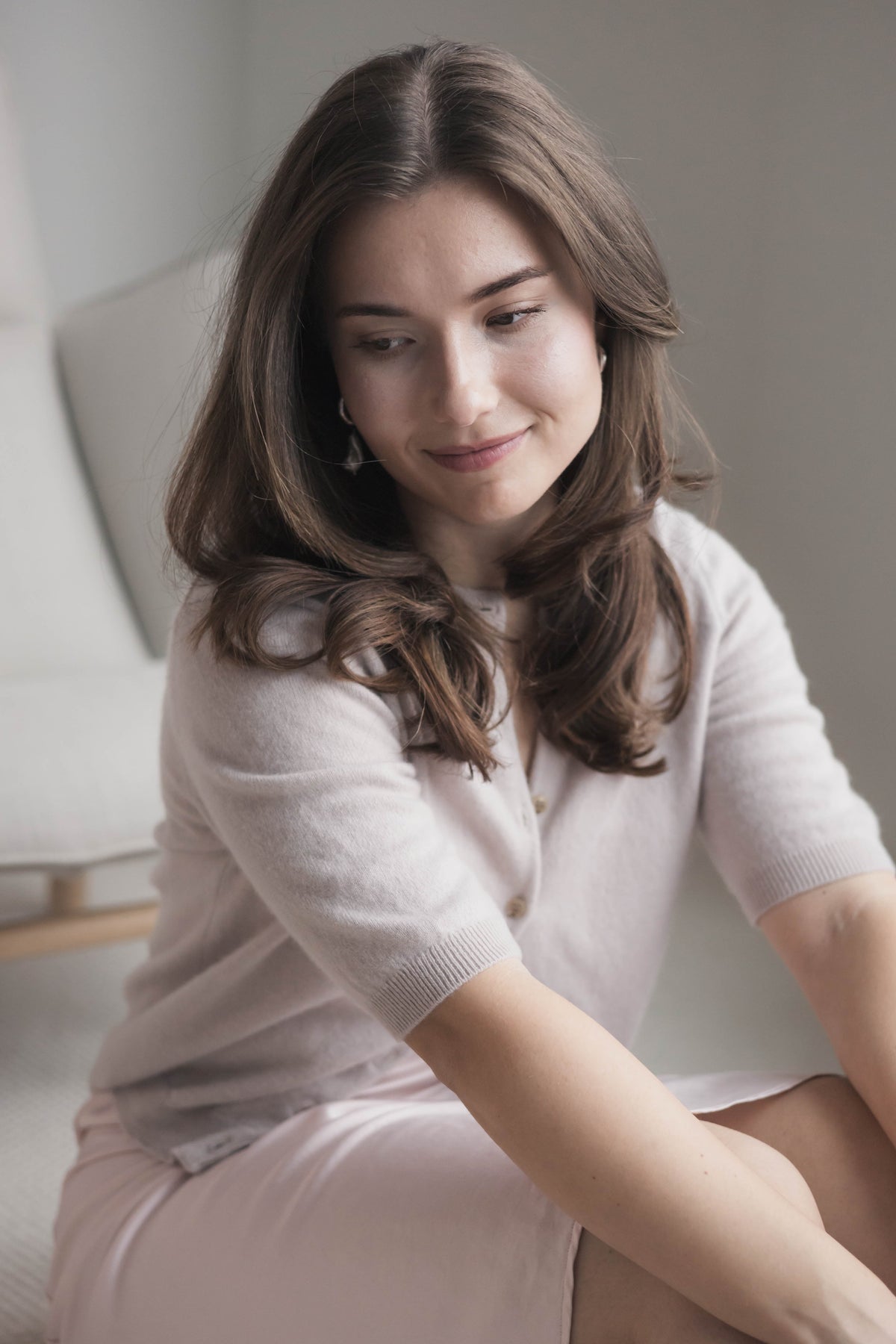 Woman sitting on a couch wearing a light pink sweater and skirt.