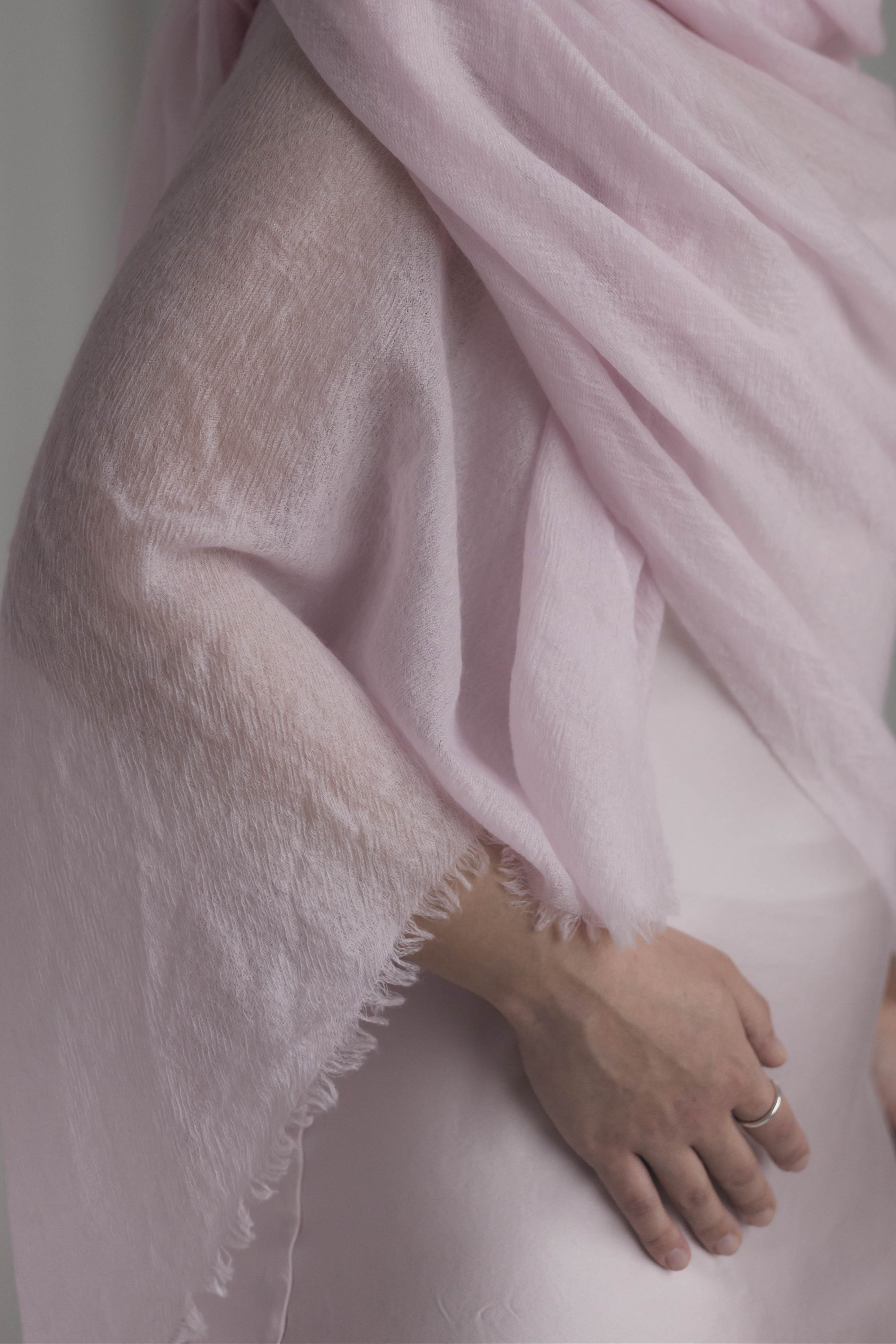 Woman wearing a light pink scarf and white dress against a neutral background