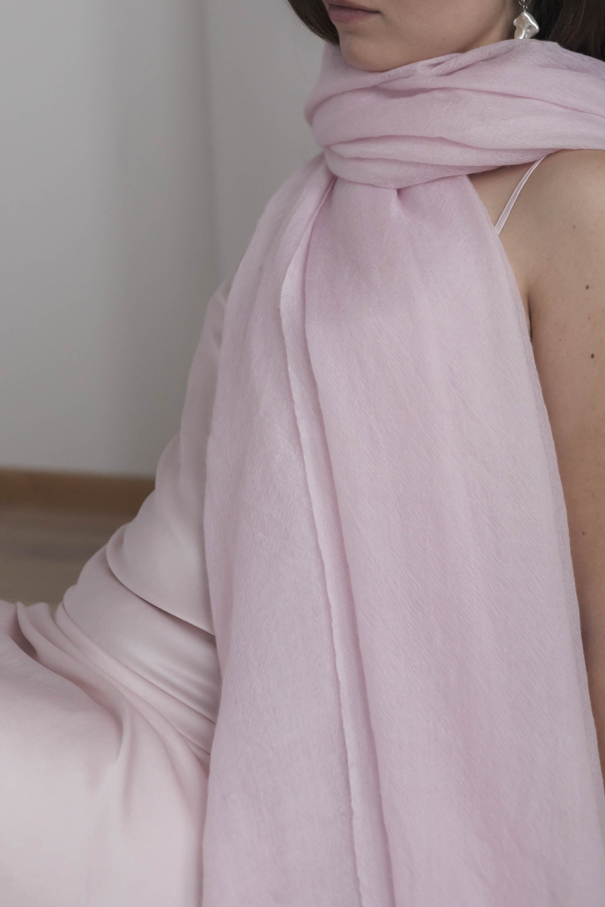 Woman wearing a light pink scarf in a minimal indoor setting